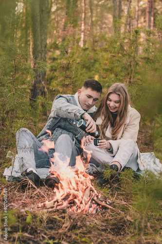  couple on a picnic in a pine forest near the fire, the guy pours the girl tea