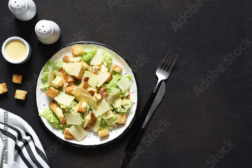 Classic Caesar salad with chicken and sauce in a plate on a concrete background, top view.