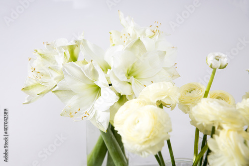 Bouquet of white lilies in a tall glass vase on a beige table against a gray wall. Copy space.