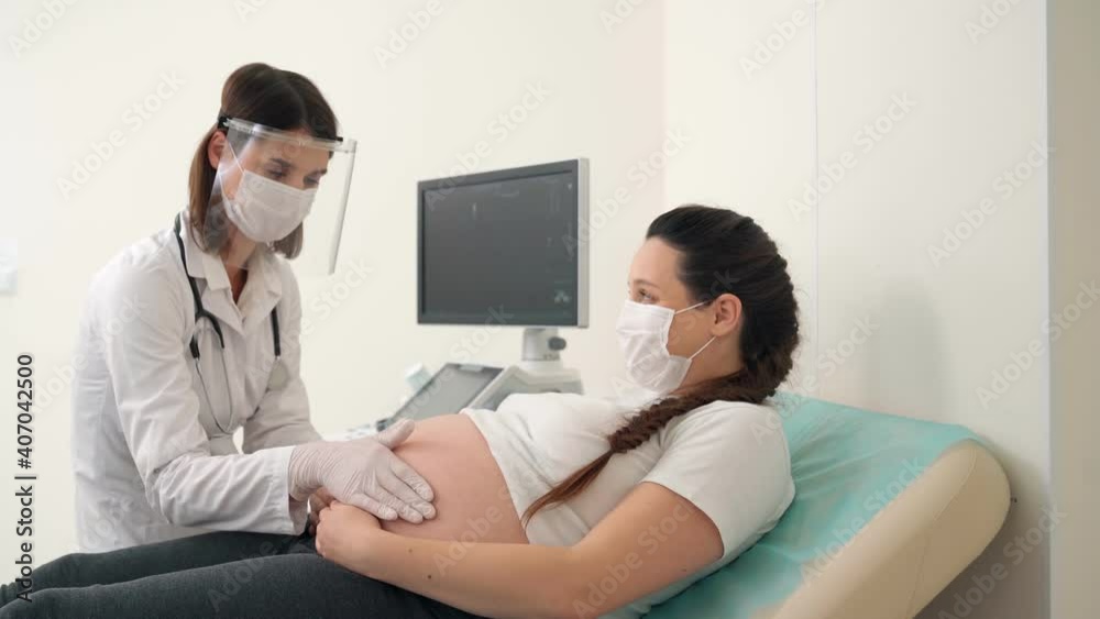 Doctor in mask and gloves examining tummy of pregnant woman Doctor in mask and gloves examining tummy of pregnant woman