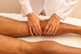 Mãos de terapeuta que está fazendo massagem em perna de paciente.