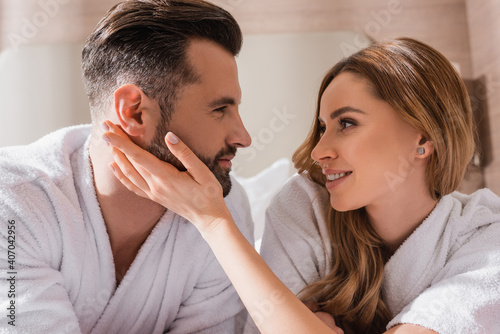 Smiling woman in bathrobe touching face of boyfriend in hotel room
