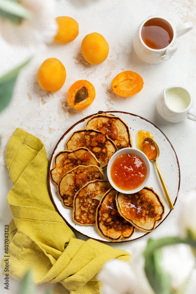 Homemade delicious pancakes with fresh apricot fruit and jam on a light slate, stone or concrete background. Top view with copy space. Homemade delicious pancakes with fresh apricot fruit and jam on a light slate, stone or concrete background. Top view with copy space.