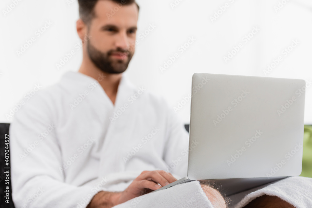 Laptop on laps of man in bathrobe on blurred background in hotel room Laptop on laps of man in bathrobe on blurred background in hotel room