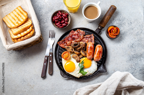 English Breakfast with fried eggs, sausages, bacon, beans, toasts, tomatoes and mushrooms on grill pan, concrette background, Top view photo