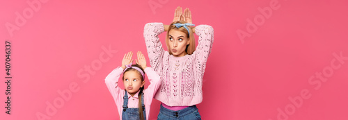 Mother and daughter making bunny ears with hands isolated on pink  banner