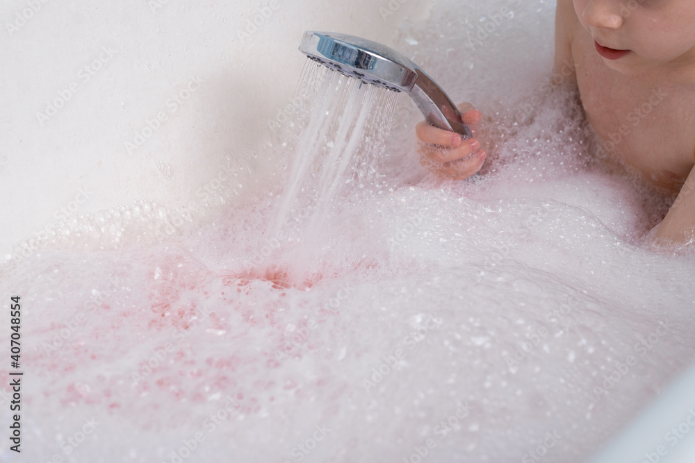 Fototapeta premium The child makes lather in the bath with the shower. Taking a bath, hygiene procedures.