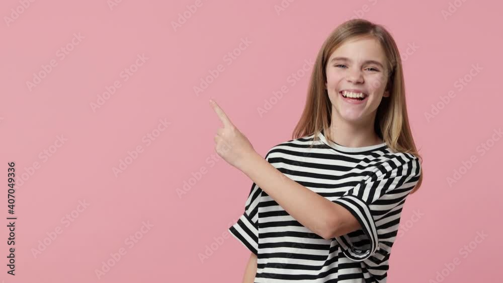 Surprised excited little kid girl 12-13 in striped t-shirt isolated on pastel pink color background studio. Childhood lifestyle concept. Pointing index finger aside up showing thumbs up like gesture Surprised excited little kid girl 12-13 in striped t-shirt isolated on pastel pink color background studio. Childhood lifestyle concept. Pointing index finger aside up showing thumbs up like gesture