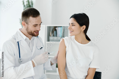 a professional doctor injects a vaccine into the shoulder of a woman in a white t-shirt on a light background