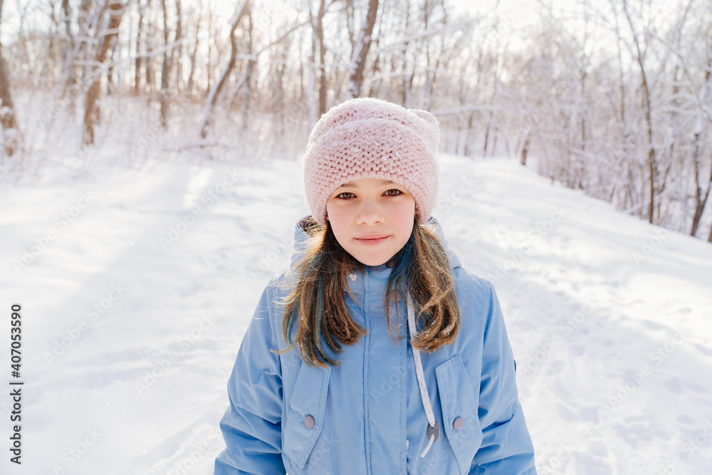 A teenage girl in a blue coat and pink hat stands in a snow-covered forest. walks in the park with children in the frosty winter weather. A teenage girl in a blue coat and pink hat stands in a snow-covered forest. walks in the park with children in the frosty winter weather.