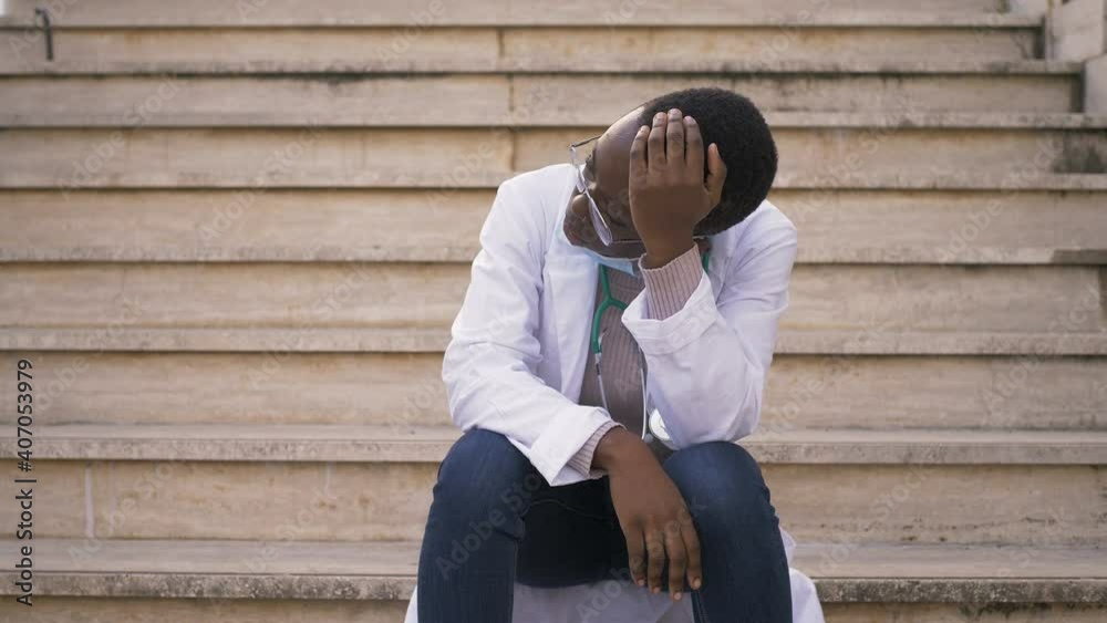 covid19 - stressed black doctor on break sitting on the stairs of the hospital covid19 - stressed black doctor on break sitting on the stairs of the hospital