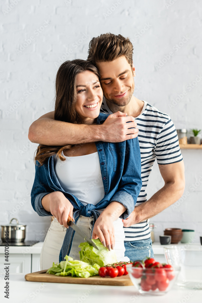 happy man hugging woman preparing salad in kitchen happy man hugging woman preparing salad in kitchen