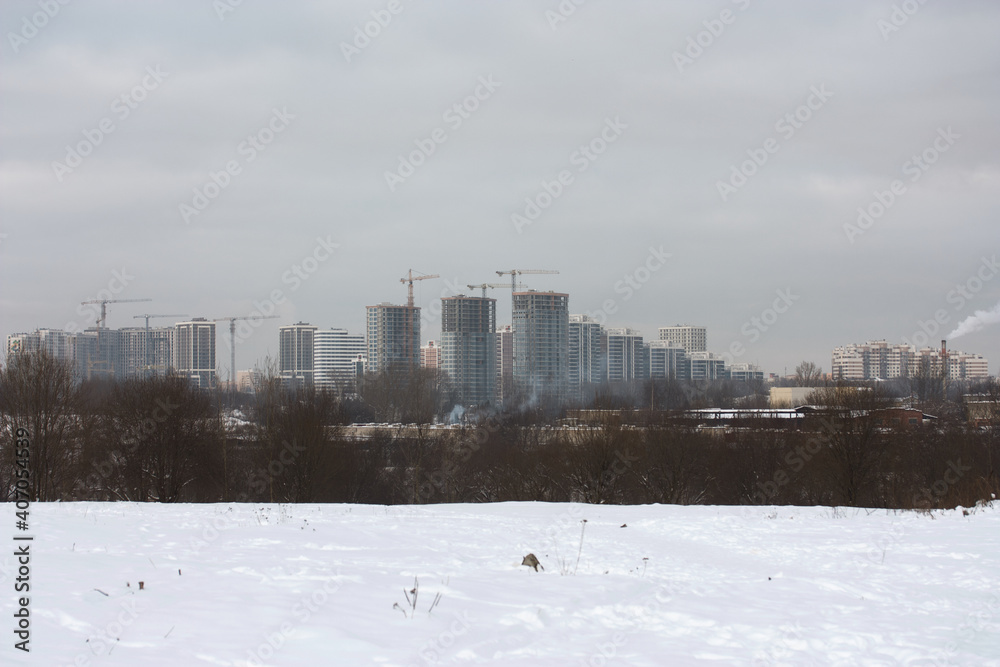 Winter city landscape. Wasteland covered with snow. On the horizon are high-rise buildings.