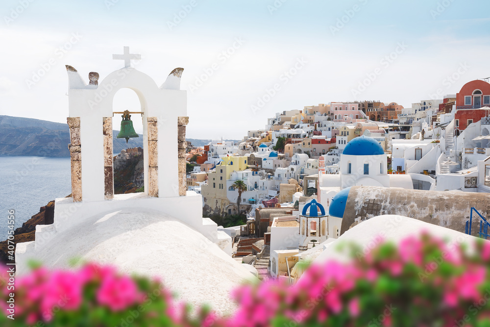 Naklejka premium Oia village through flowers and traditional Greek white church arch with cross and bells in Oia village of Cyclades Island, Santorini