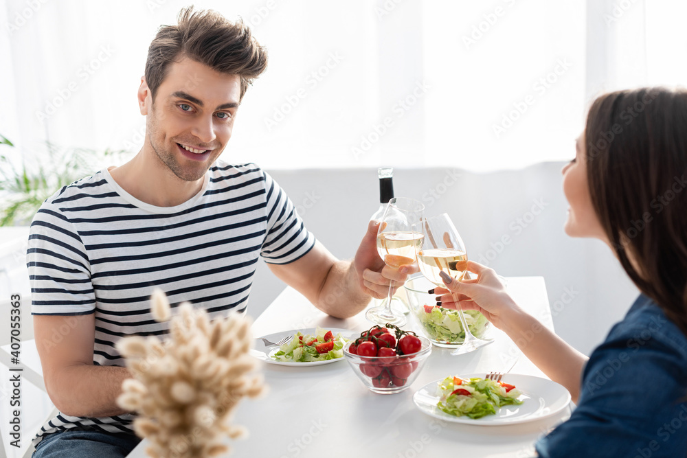 cheerful man and woman toasting glasses of wine near lunch on table