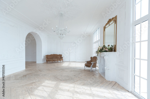 chic white huge spacious hall with a minimum of expensive antique furniture. Baroque interior design with ornament on the walls and parquet on the floor.