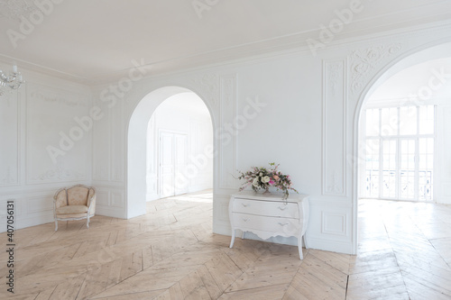 chic white huge spacious hall with a minimum of expensive antique furniture. Baroque interior design with ornament on the walls and parquet on the floor.