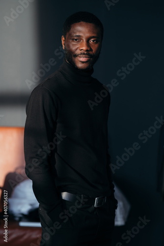 Portrait of attractive stylish african american man in black turtleneck standing in sunbeams and posing for a photo
