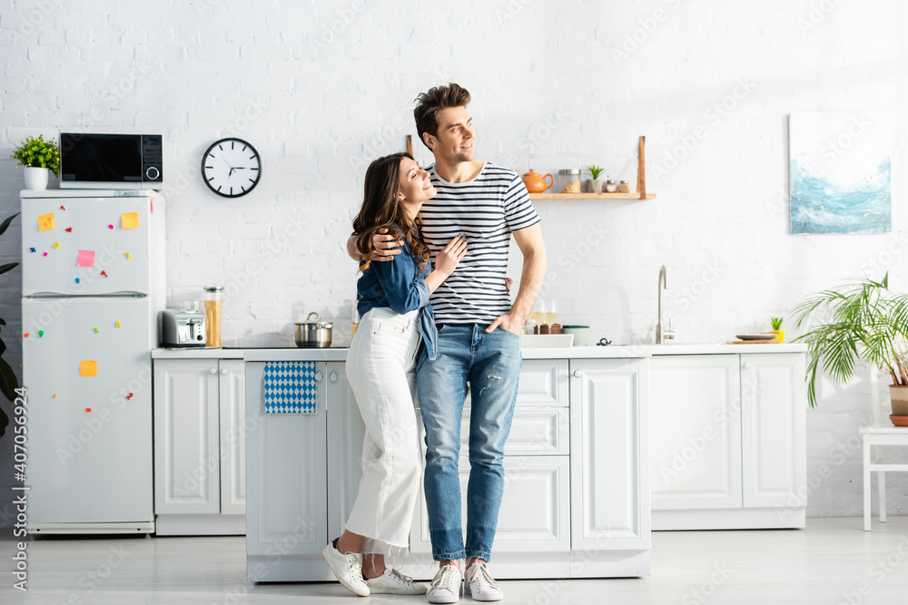 full length of happy woman hugging cheerful man standing with hand in pocket in modern kitchen full length of happy woman hugging cheerful man standing with hand in pocket in modern kitchen
