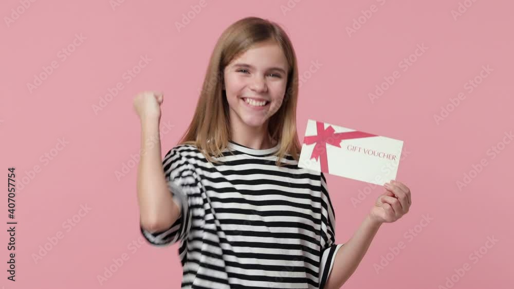 Cheerful excited little blonde kid girl 12-13 in striped t-shirt isolated on pink background studio. Childhood lifestyle concept. Pointing index finger on gift certificate on you doing winner gesture Cheerful excited little blonde kid girl 12-13 in striped t-shirt isolated on pink background studio. Childhood lifestyle concept. Pointing index finger on gift certificate on you doing winner gesture