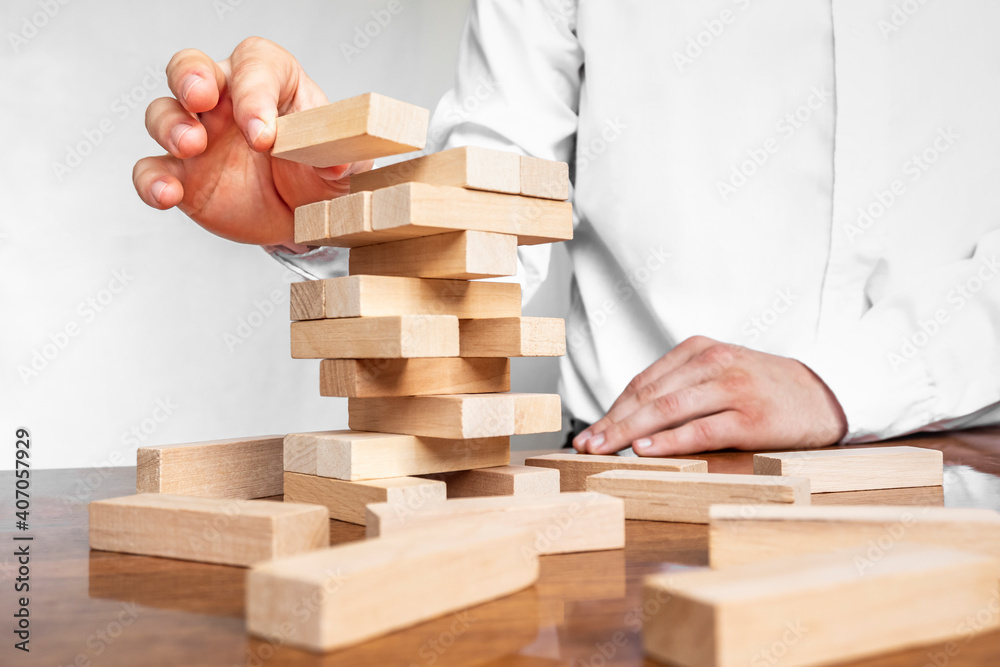 Planning, risk and strategy in business, businessman gambling placing wooden block on a tower. The tower from wooden blocks and man's hand take one block Planning, risk and strategy in business, businessman gambling placing wooden block on a tower. The tower from wooden blocks and man's hand take one block