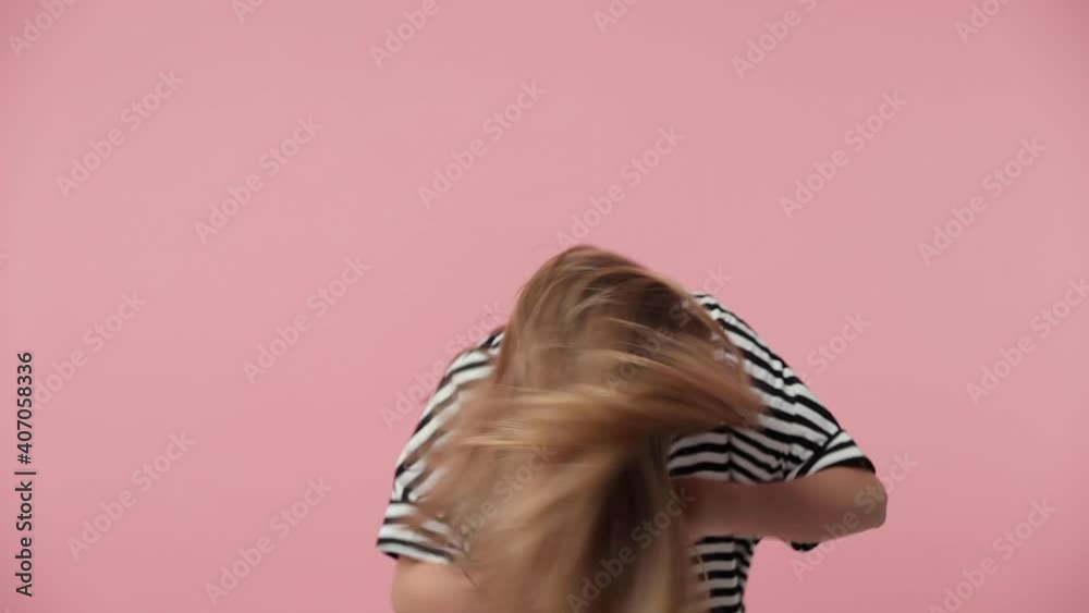 Slow motion funny laughing little blonde kid girl 12-13 years old in casual striped t-shirt isolated on pink background studio. Childhood lifestyle concept. Dancing shaking head with fluttering hair