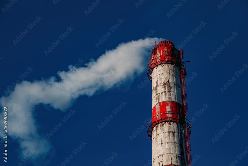 Red and white smoking industrial pipe against the blue sky Red and white smoking industrial pipe against the blue sky