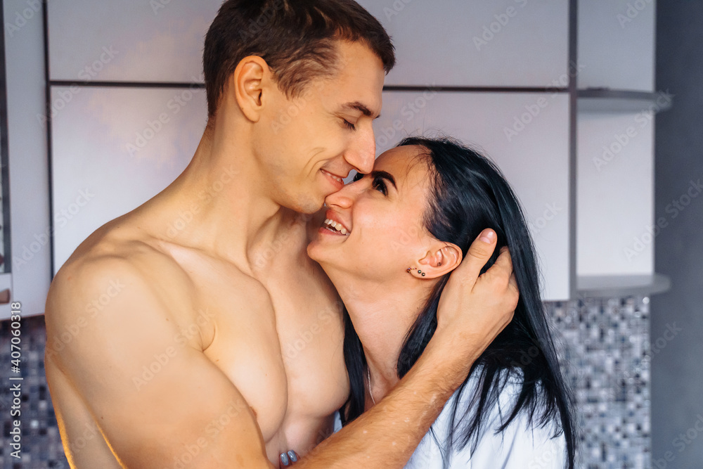 Close-up of a laughing couple in love. Guy and girl hugging tenderly in the kitchen. Foreplay before hot sex, at night. Joking, smiling at each other in the soft, warm yellow light