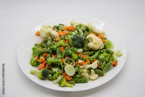 Frozen vegetables: cauliflower, green peas, leeks, broccoli, carrots, green beans on a white plate.