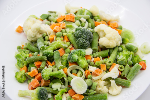 Frozen vegetables: cauliflower, green peas, leeks, broccoli, carrots, green beans on a white plate.