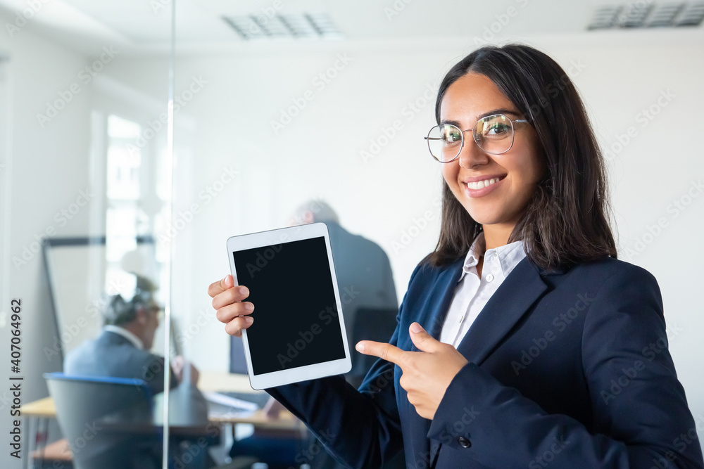 Happy confident business lady holding tablet, showing and pointing finger at blank screen, looking at camera and smiling. Copy space. Communication and advertising concept Happy confident business lady holding tablet, showing and pointing finger at blank screen, looking at camera and smiling. Copy space. Communication and advertising concept