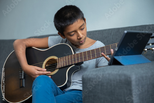 mexican boy taking guitar lessons at home due to coronavirus lockdown, home schooling