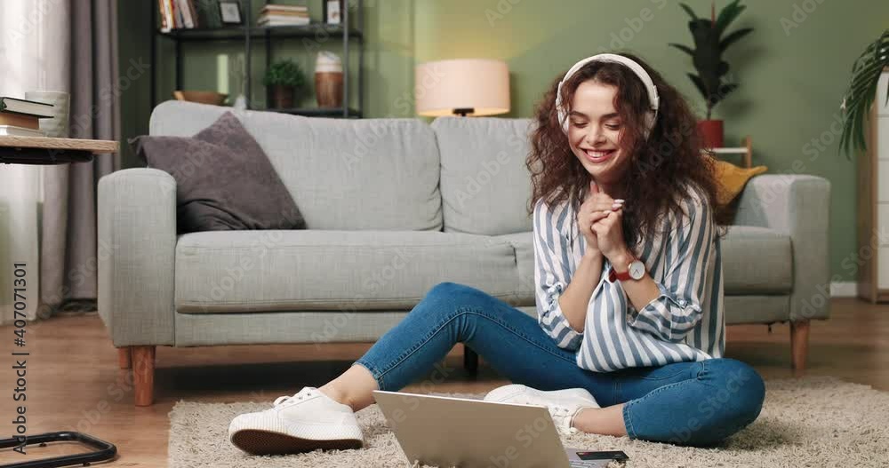 Happy young Caucasian beautiful woman sitting on floor in cozy home listening to music or watching movie in headphones on laptop, having fun, feeling joy clapping her hands. leisure concept Happy young Caucasian beautiful woman sitting on floor in cozy home listening to music or watching movie in headphones on laptop, having fun, feeling joy clapping her hands. leisure concept
