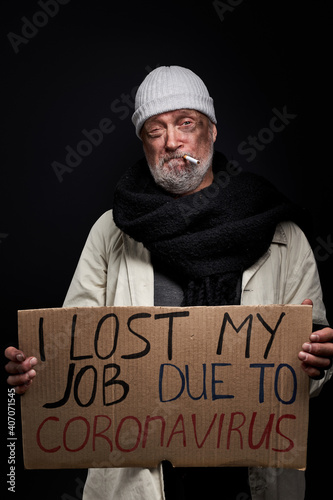 Fotografija desperate bum with cigarette in mouth stand with cardboard in hands, needs shelt