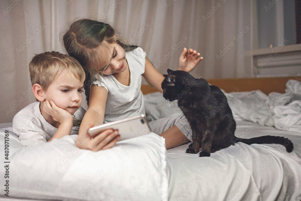 Sleepy kids in pajama watching video on smartphone in bed and struggling to sleep in the evening, healthy sleeping, invest in rest concept Sleepy kids in pajama watching video on smartphone in bed and struggling to sleep in the evening, healthy sleeping, invest in rest concept
