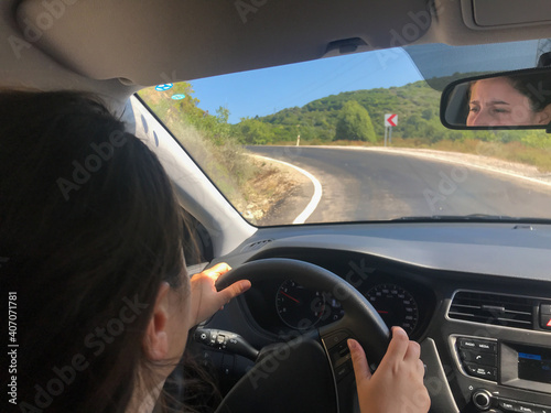 young female driver holding the steering wheel and her face appears on rearview mirror