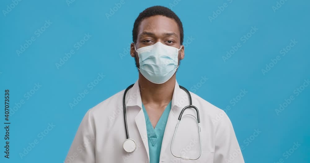 Studio portrait of black medical doctor in facemask shaking head in rejection, feeling not agree, blue background Studio portrait of black medical doctor in facemask shaking head in rejection, feeling not agree, blue background