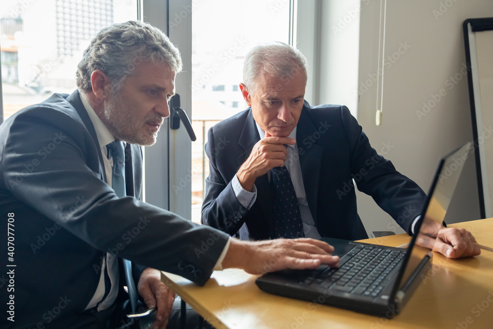 Focused grey haired businessmen looking at laptop display in office, discussing content. Business partners gathering at workplace, studying report on display together. Corporate communication concept Focused grey haired businessmen looking at laptop display in office, discussing content. Business partners gathering at workplace, studying report on display together. Corporate communication concept