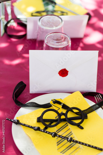 Decoración mesa de comida sobre mantel granate temática de Harry Potter, con gafas, varita y sobre.