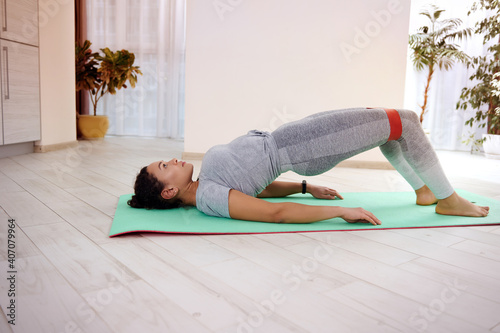 Young athlete performs a glute bridge on a fitness mat using an elastic band photo