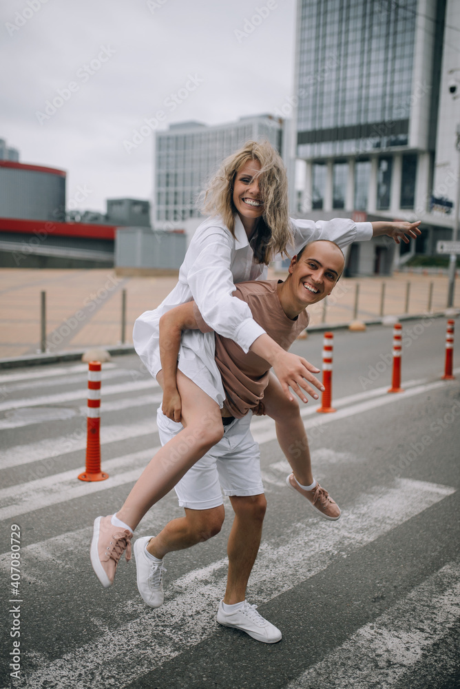 Man carrying young attractive woman on shoulders while spending time together outdoors in the city.Playful couple. Man carrying young attractive woman on shoulders while spending time together outdoors in the city.Playful couple.