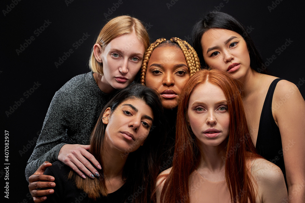 Fototapeta premium mixed race group of ladies isolated on black background, young women of different ethnicity seriously looking at camera