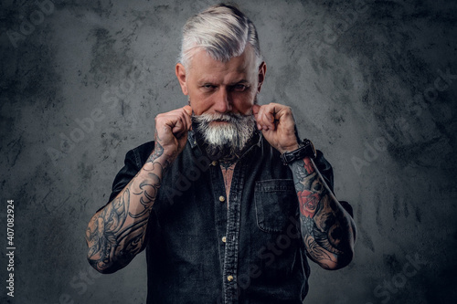 Fotografi Portrait of old and confident man with tattooed body and gray hairs which poses in dark background