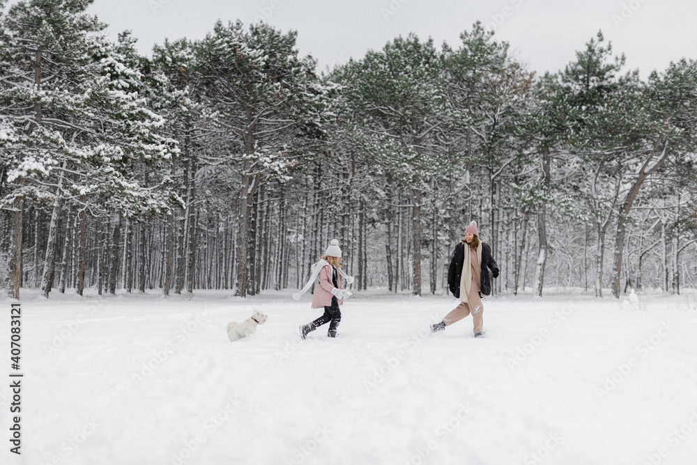 mother and daughter walk in winter forest with dog