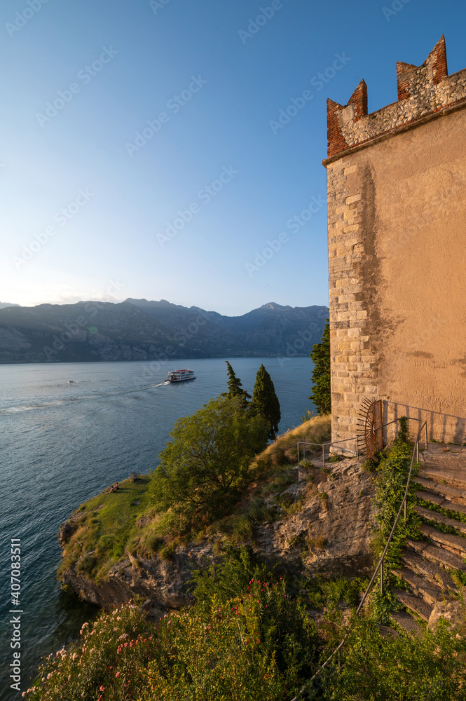 Lake Garda from Malcesine seen from the castle with the reflections of the sun on its waters on a hot day in late summer. Beautiful and romantic sunset. Verona, Veneto, Italy.