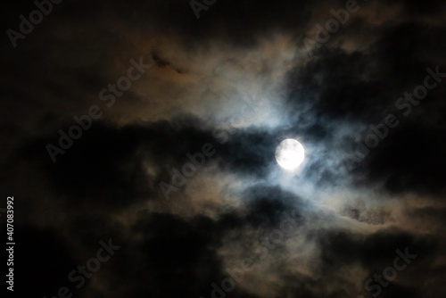 The full moon hiding in the cloudy night sky. Dark background of the moonlight and clouds