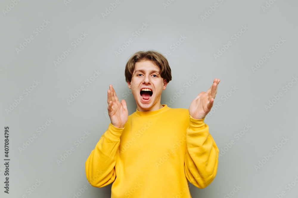 Joyful guy stands on a background of a gray wall with his mouth open and looks into the camera with a happy face, wearing yellow clothes, isolated. Joyful guy stands on a background of a gray wall with his mouth open and looks into the camera with a happy face, wearing yellow clothes, isolated.