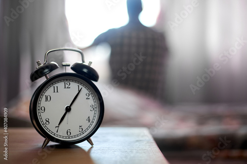 alarm clock in bedroom and a young man after waking up, sunlight in morning.