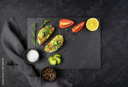 Two avocado sandwiches, tomatoes, lemon and rosemary on a flat plate on a black concrete background. Top view, with space to copy. The concept of healthy food.
