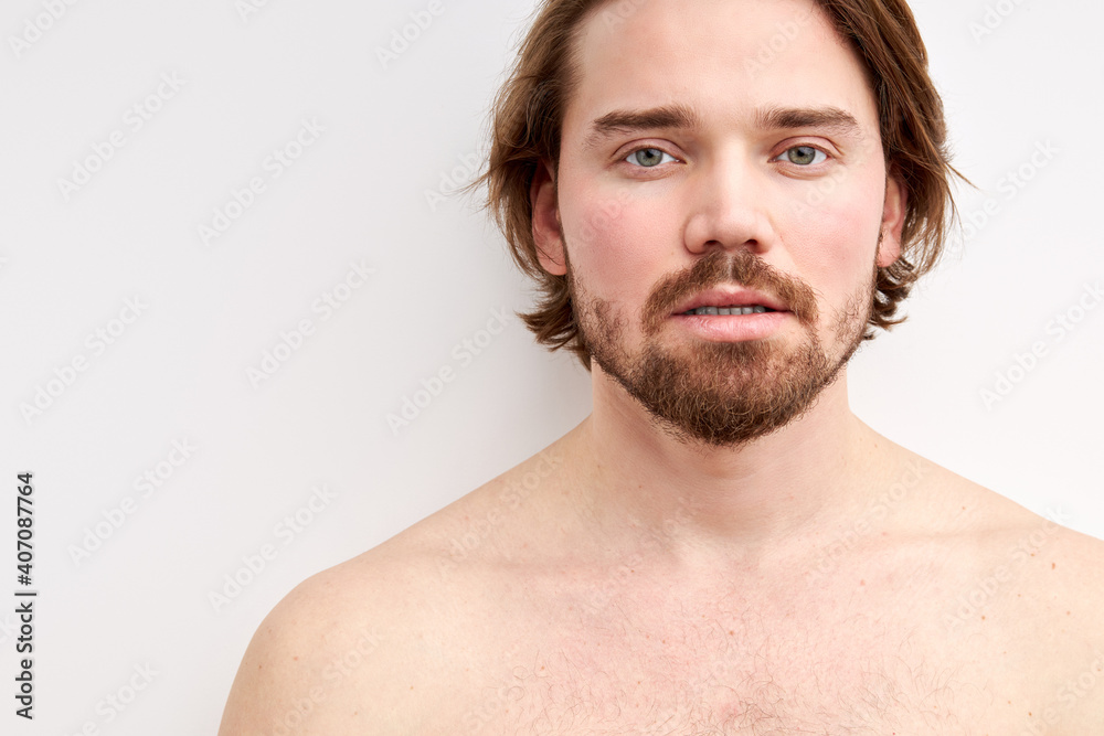 Obraz premium shirtless male with long hair and beard posing at camera, half-naked man looks at camera, calm and serious. isolated white backrgound